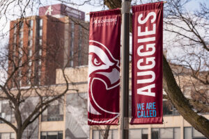 Two maroon Augsburg banners in winter. The left banner is an Auggie the eagle graphic and the right says "We Are Called Auggies." 